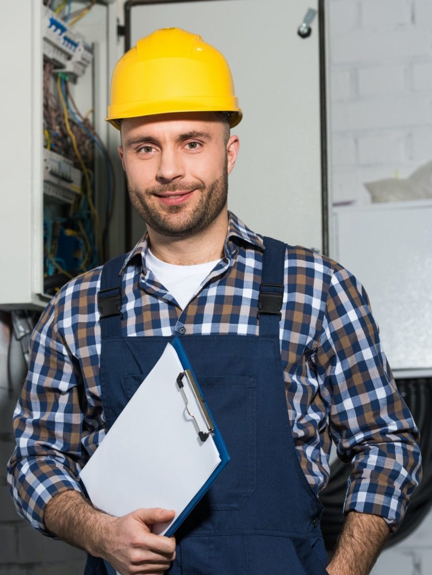 electrician holding clipboard and smiling by electrical box e1651083769975.jpg